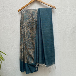 Ambi Printed Tissue Silk Saree in Tussar and teal blue with a bold paisley print, on a wooden hanger
