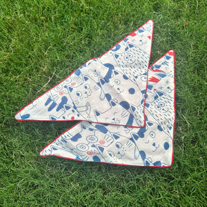 Navy and cream illustrated cat print cotton bandana with red border detail, photographed on green grass, by The Thread Weavers