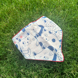 Navy and cream illustrated cat print cotton bandana with red border detail, photographed on green grass, by The Thread Weavers