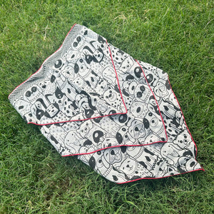Black and white illustrated dog print cotton bandana with red border, photographed on green grass, by The Thread Weavers