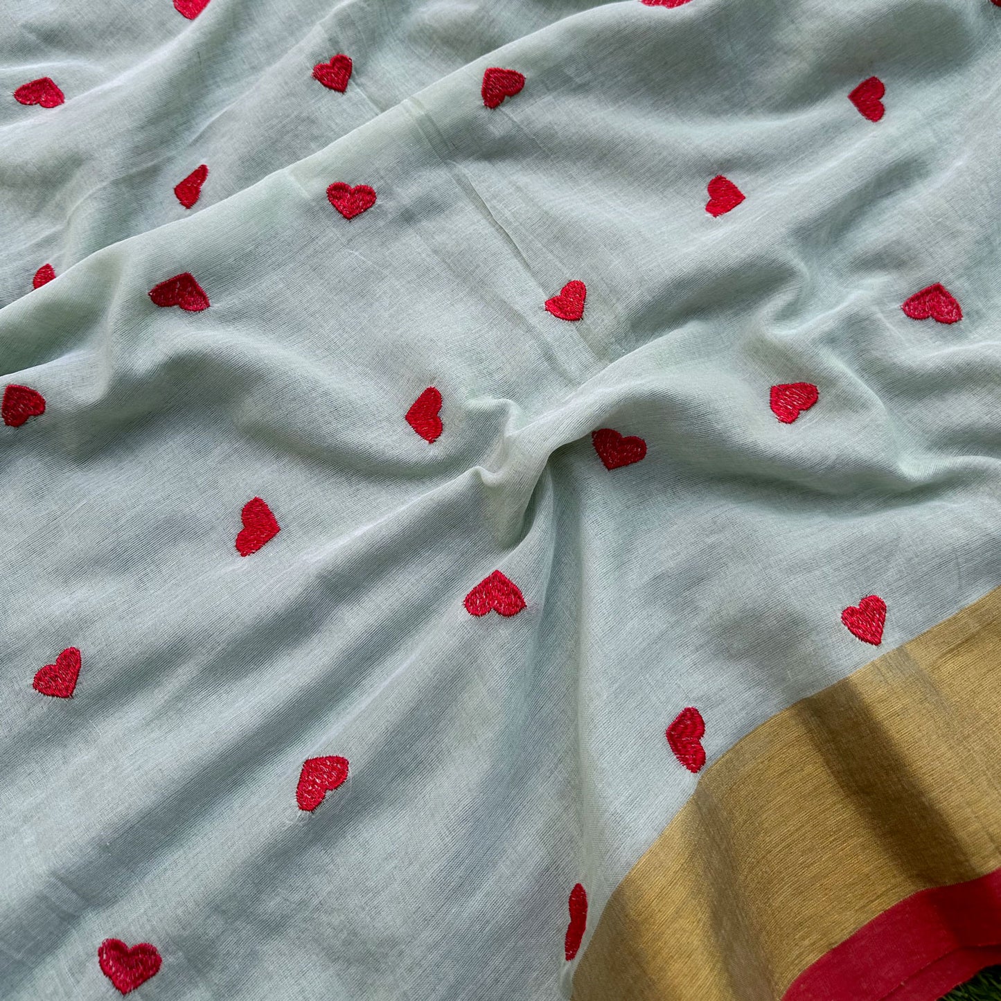 Delicate embroidered heart motifs on a mint green mul cotton saree with gold border detailing.