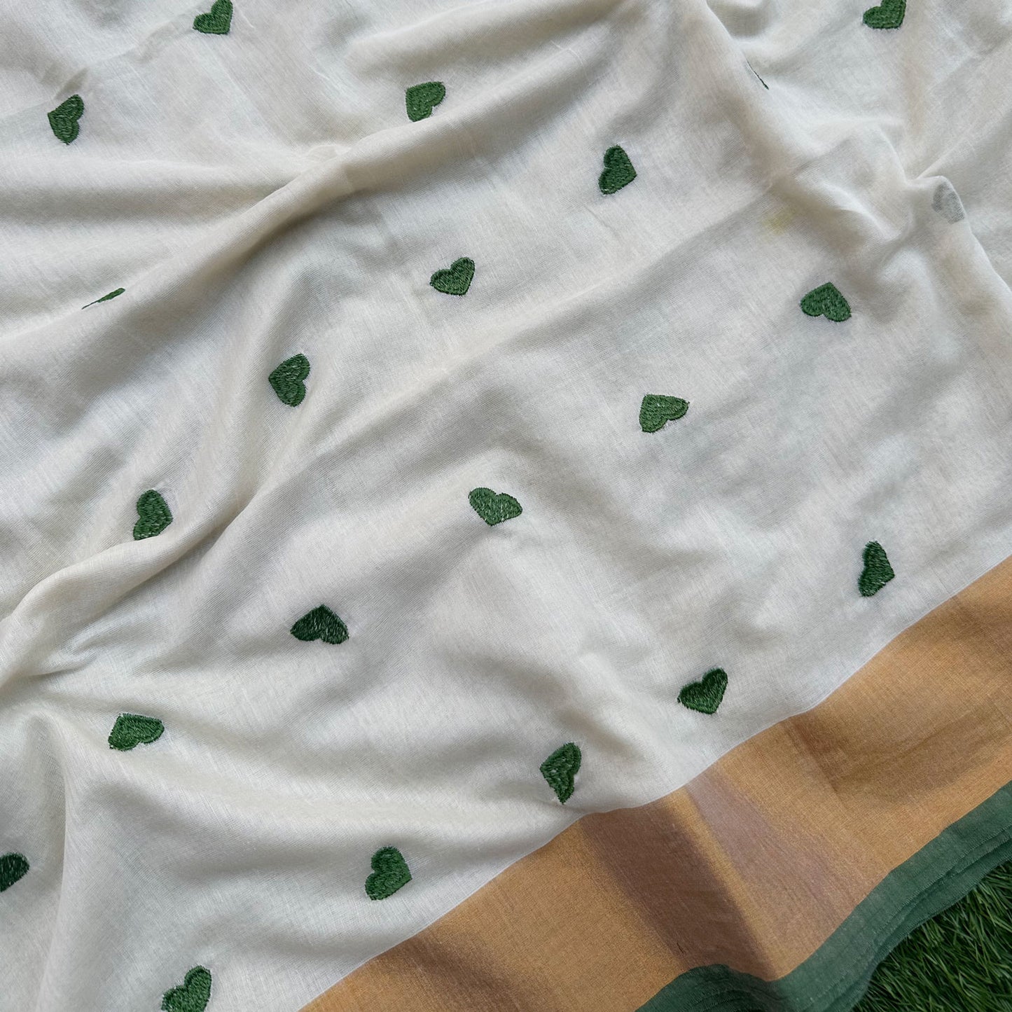 Delicate green heart embroidery on an ivory mul cotton saree with subtle gold border accents.