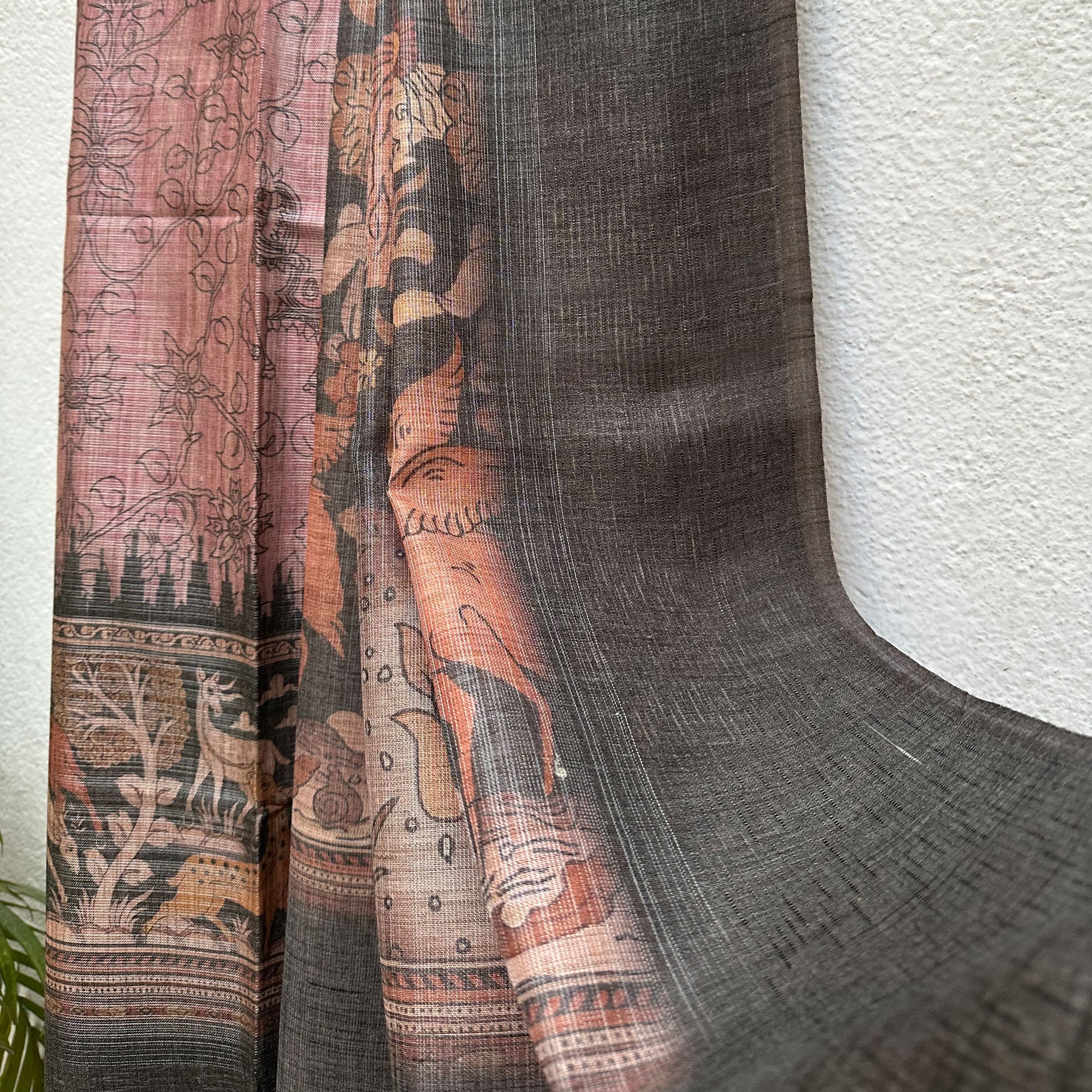 Closeup of the pallu with charcoal solid border and kalamkari jaal pattern body, on a wooden hanger