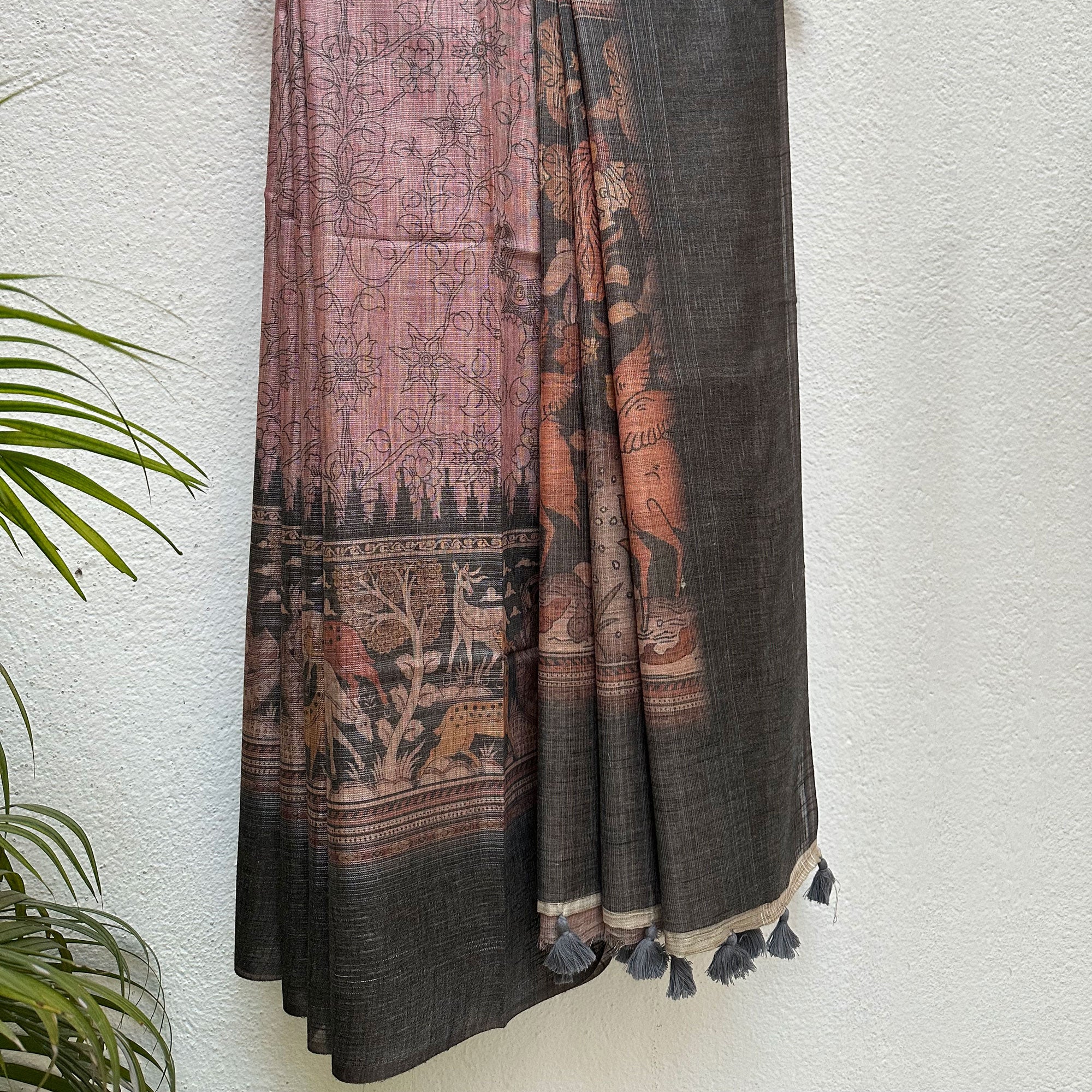 Closeup of the forest print border with charcoal solid border and kalamkari jaal pattern body, on a wooden hanger