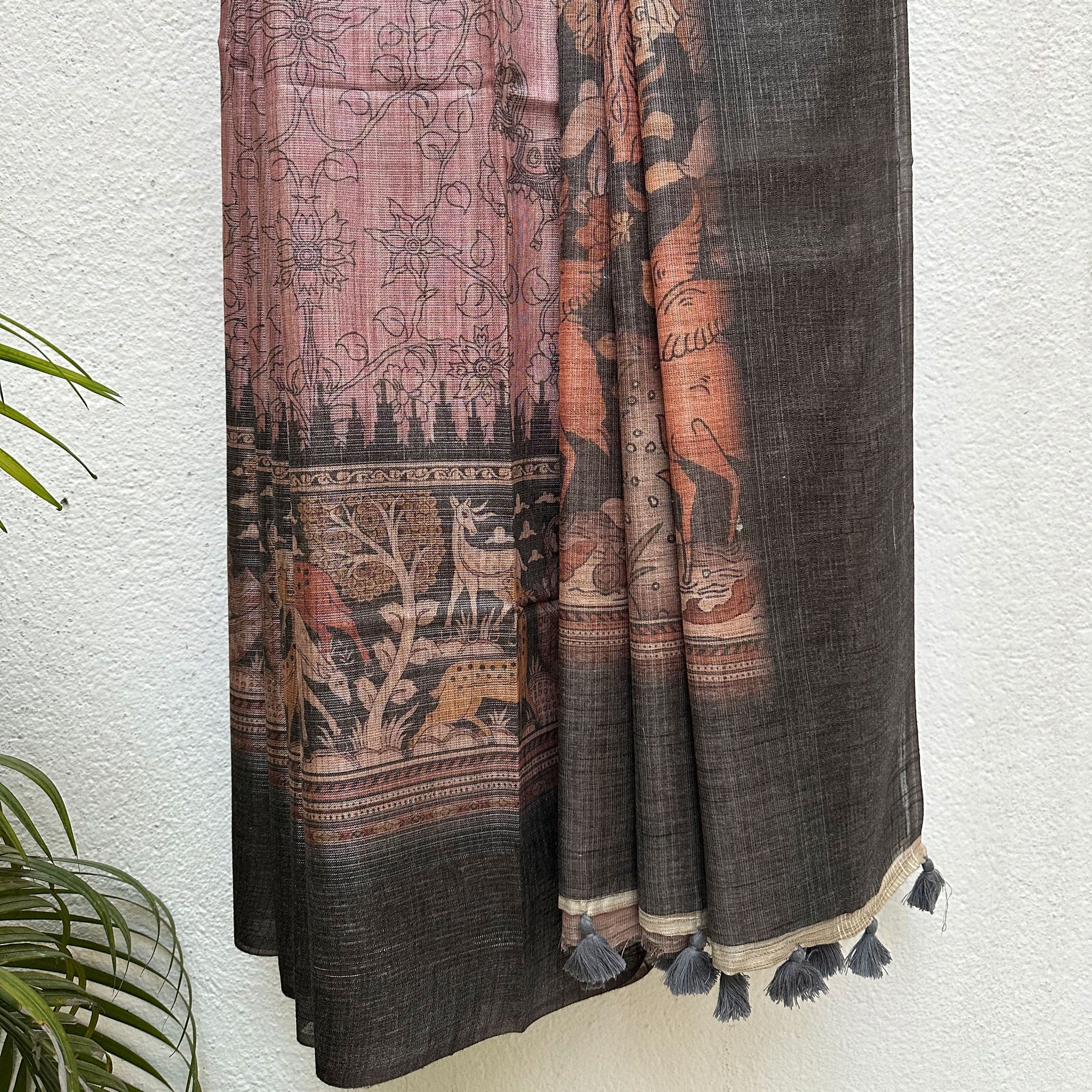 Closeup of the forest print border with charcoal solid border and kalamkari jaal pattern body, on a wooden hanger