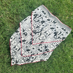 Black and white illustrated dog print cotton bandana with red border, photographed on green grass, by The Thread Weavers