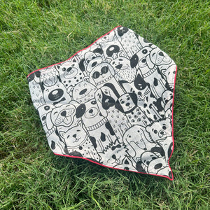 Black and white illustrated dog print cotton bandana with red border, photographed on green grass, by The Thread Weavers