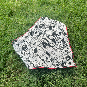 Black and white illustrated dog print cotton bandana with red border, photographed on green grass, by The Thread Weavers