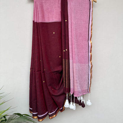 Contemporary mul cotton saree featuring a rich wine body, blush pink pallu, subtle sequins and tassel detailing.