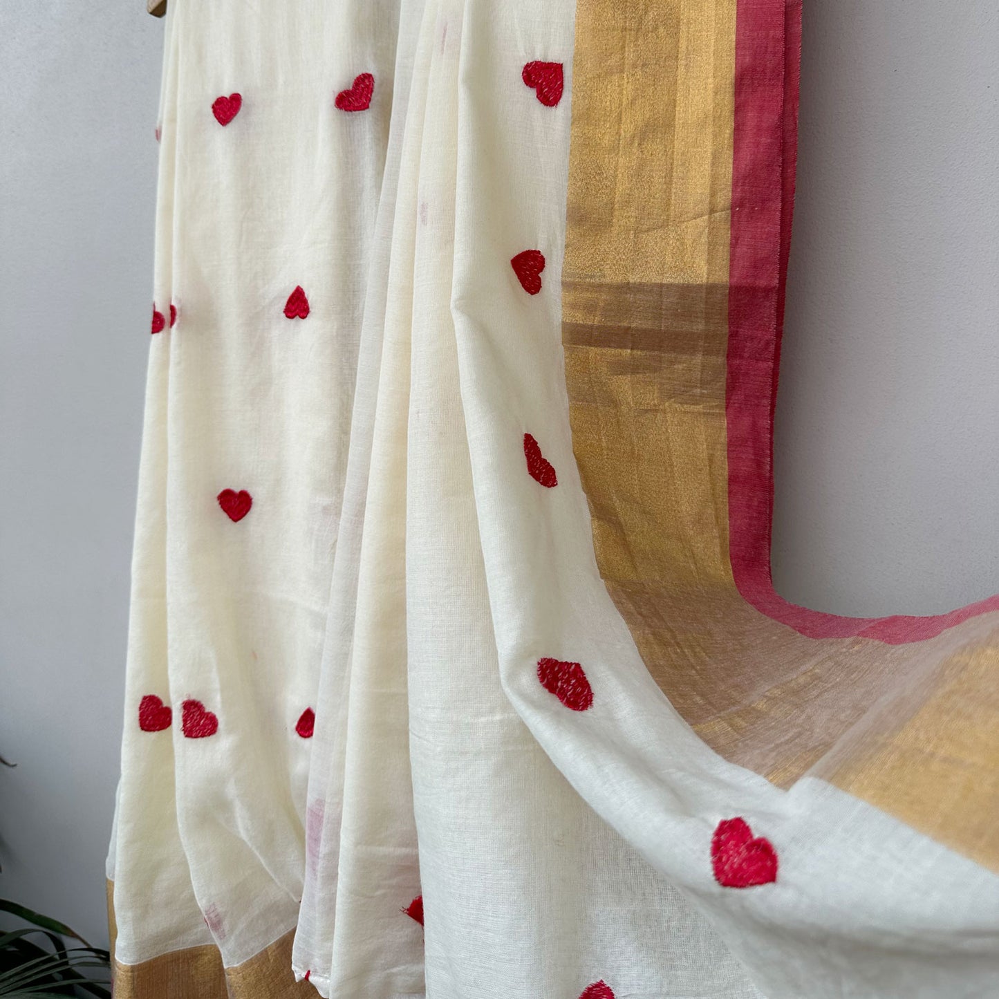 Contemporary ivory mul saree featuring delicate red heart embroidery, soft drape and artistic tassel detailing.