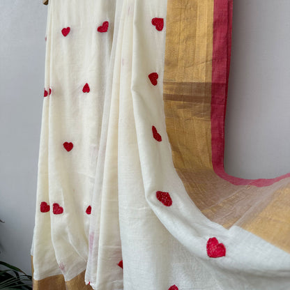 Contemporary ivory mul saree featuring delicate red heart embroidery, soft drape and artistic tassel detailing.