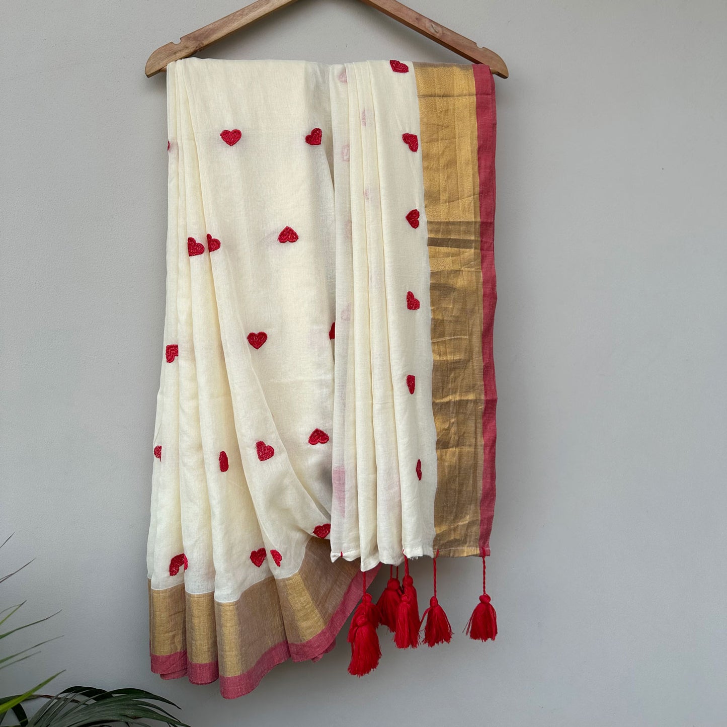 Handcrafted ivory embroidered saree with red heart motifs, contrast red border and contemporary Indian design.