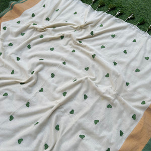 Delicate green heart embroidery on an ivory mul cotton saree with subtle gold border accents.
