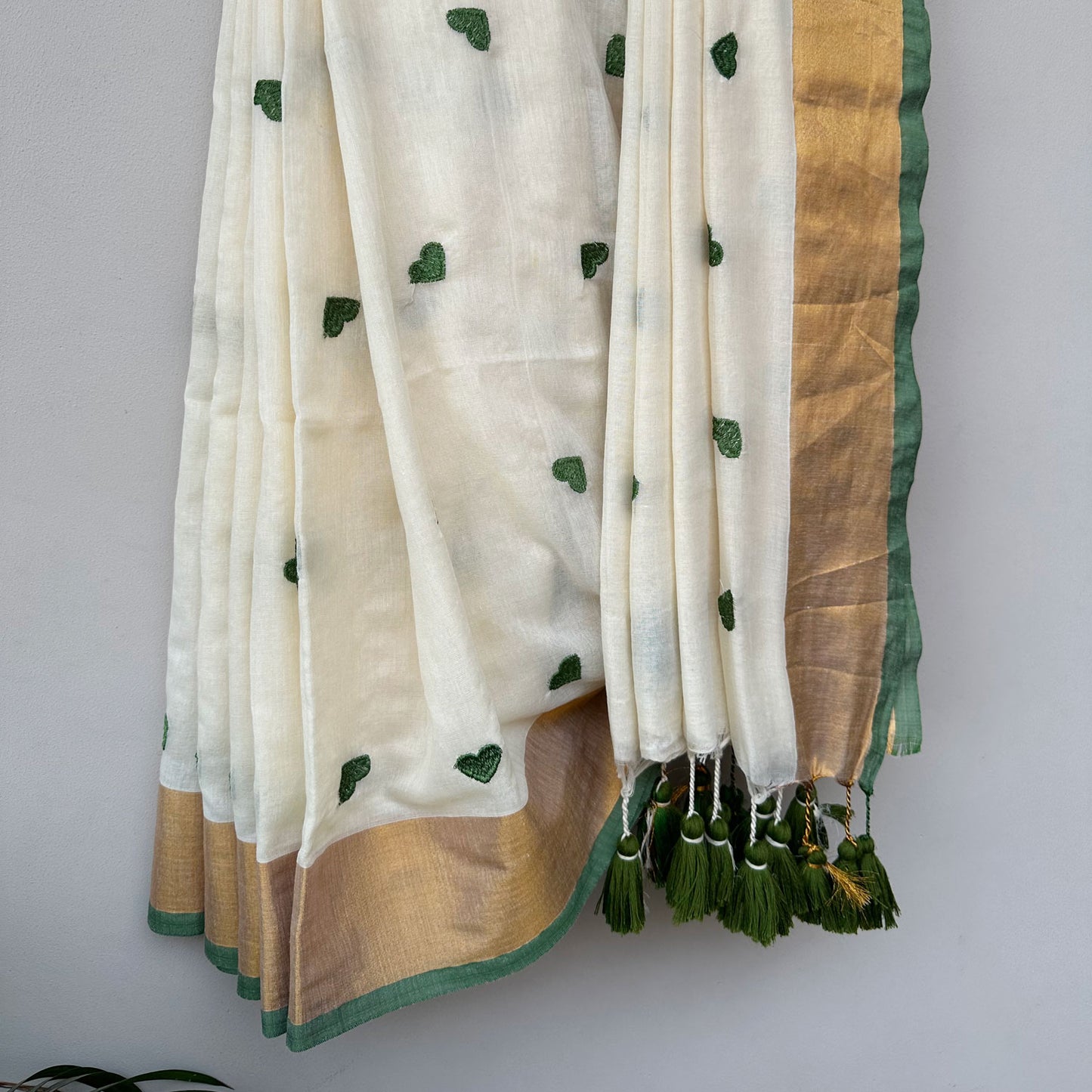 Contemporary ivory mul saree featuring delicate green heart embroidery and earthy olive-toned accents.