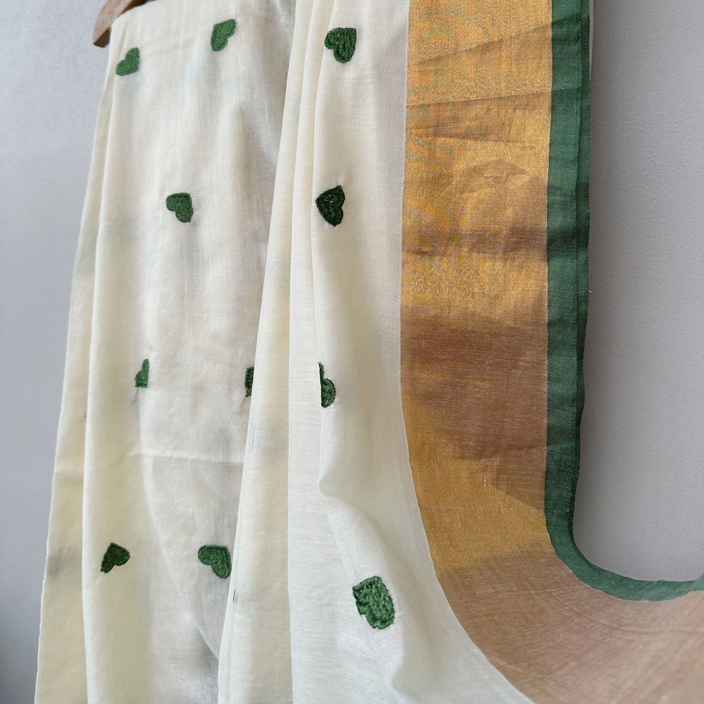 Lightweight mul cotton saree in ivory with scattered green heart motifs and elegant gold border detailing.