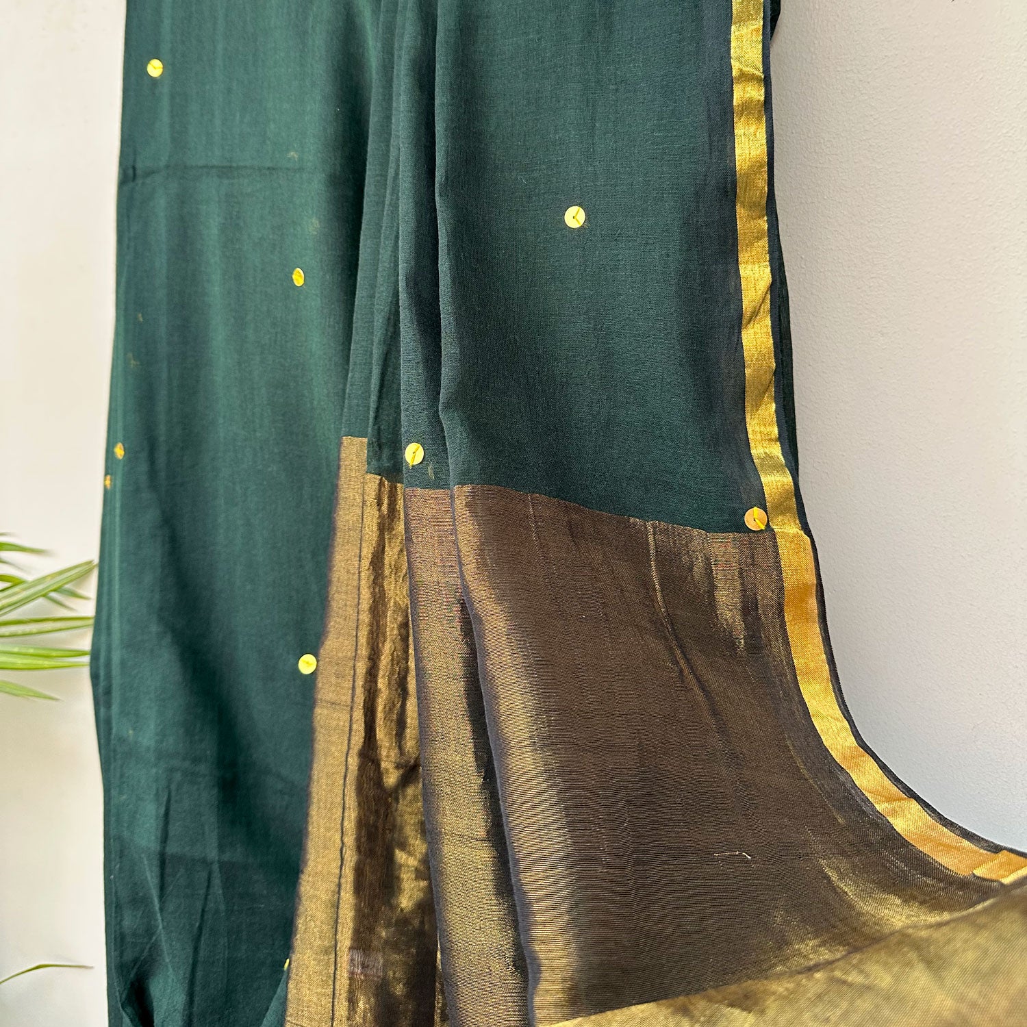 Handcrafted green mul cotton saree with delicate sequins, contrast border and modern Indian styling.